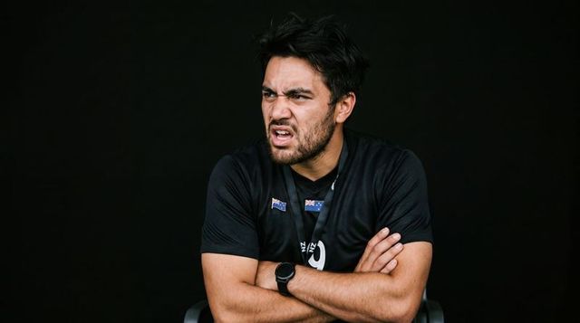 Frustrated male coach grimacing with arms crossed in black sports tee and lanyard