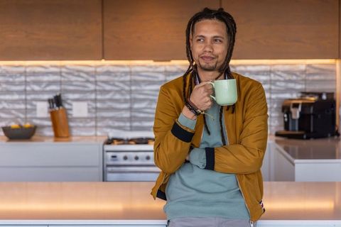 Relaxed african american man with dreadlocks holding coffee mug in modern kitchen