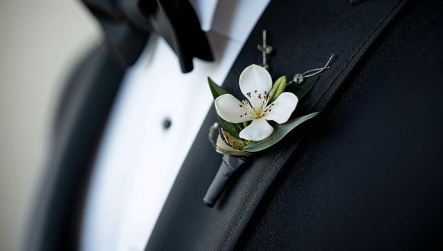 Groom wearing black tuxedo at wedding with white blossom boutonniere on left lapel closeup