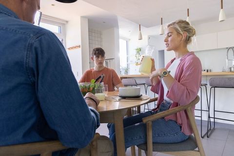 Family sharing relaxed breakfast conversation at dining table, woman pouring lemonade
