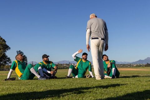 Baseball players listening to coach on outfield grass during sunny team practice session