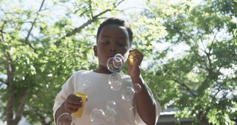 Sunlit backyard moment african american boy blowing bubbles holding yellow bottle and wand