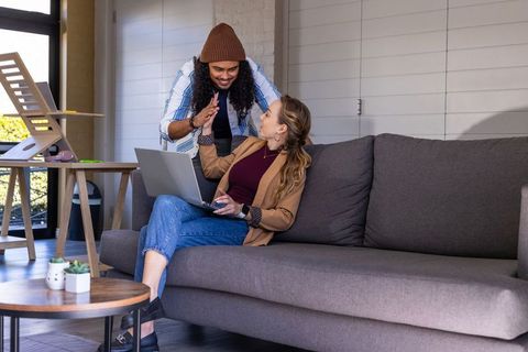 Couple collaborating on laptop, high-fiving on sofa in cozy modern home workspace