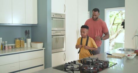 African american father helping schoolboy with backpack in modern kitchen morning routine