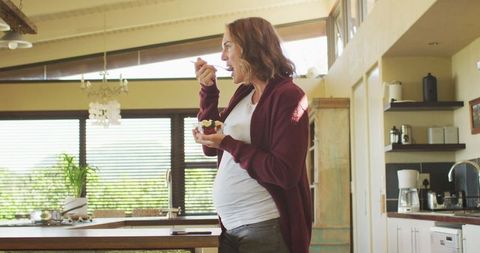 Pregnant Woman Eating Ice Cream in Sunlit Kitchen