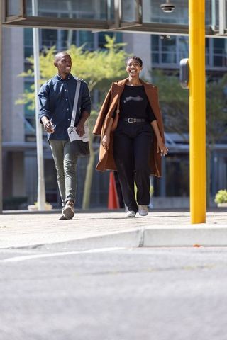 African american friends walking downtown smiling in brown coat and casual business wear