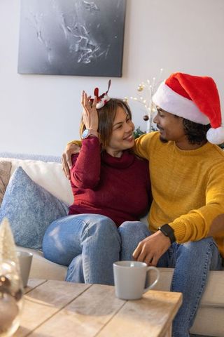 Couple wearing santa hat and reindeer headband on cozy couch sharing warm holiday moment