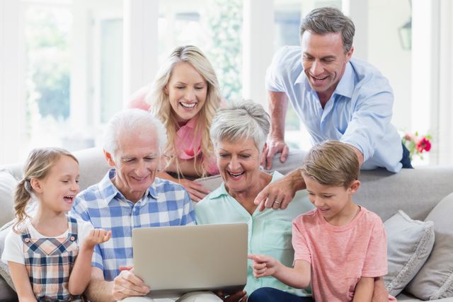 Multi-generation family gathered in living room, engaging with laptop. Grandparents, parents, and children smiling and bonding over technology. Ideal for illustrating family togetherness, digital lifestyle, and intergenerational connections in a home setting.