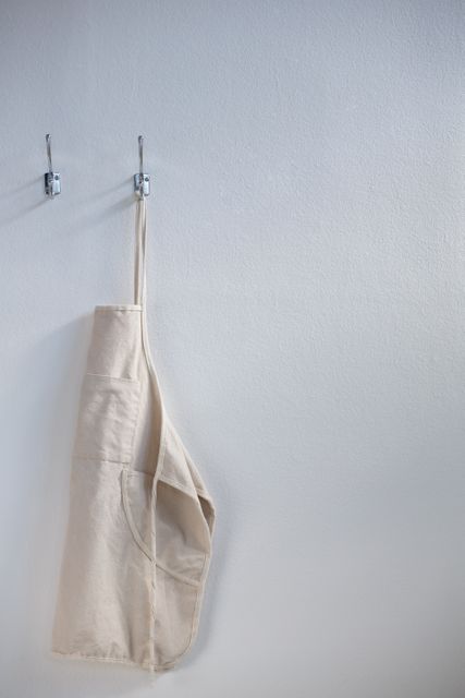 Apron hanging on a hook against a white wall, ideal for illustrating concepts of home organization, kitchen decor, and minimalist living. Perfect for use in articles, blogs, or advertisements related to cooking, home improvement, and interior design.