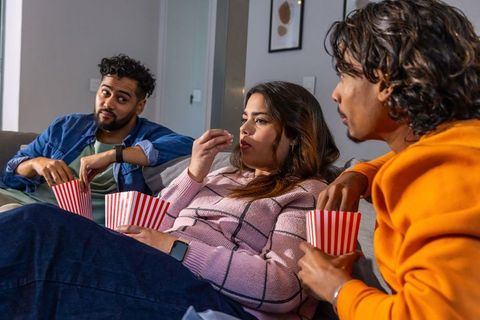 Diverse friends relaxing on couch eating popcorn and watching movie night together