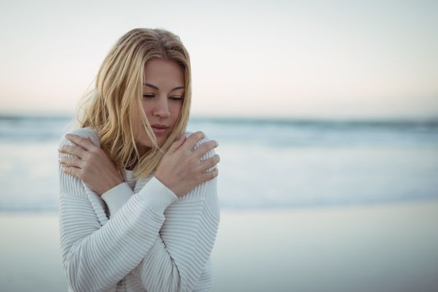 Young woman with eyes closed hugging self at beach during dusk
