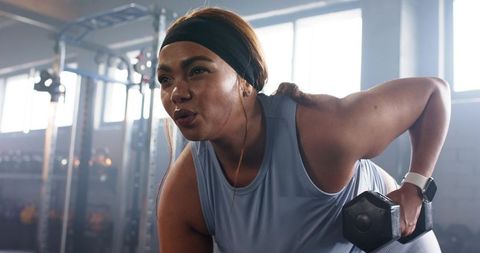 Focused African American woman lifting dumbbell during strength training wearing smartwatch