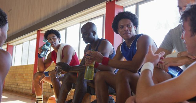 Diverse male basketball team and coach resting and drinking water after match. basketball, sports training at an indoor court.