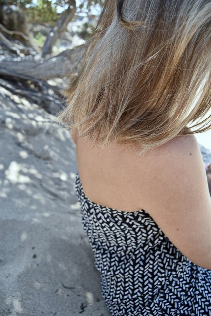 Woman enjoying a peaceful moment sitting on a sandy beach. The image might be used in travel brochures, summer vacation promotions, lifestyle blogs, or wellness articles emphasizing relaxation and outdoor leisure.