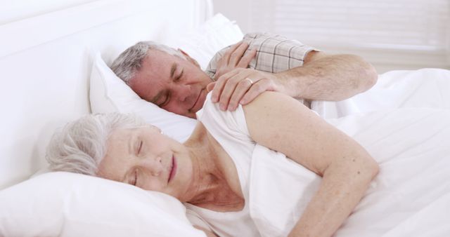 Elderly couple lying together in bed, enjoying a peaceful sleep. The senior man, with grey hair, keeping an arm around the woman, fostering a sense of security and closeness. This image can be used for themes related to senior living, intimate relationships, rest, and the importance of sleep in a healthy lifestyle. Ideal for use in healthcare, lifestyle, or retirement content marketing.