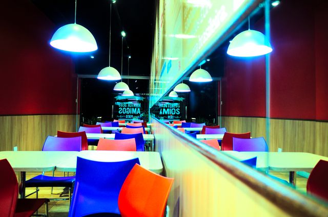Perfect for representing modern and vibrant dining areas, this lively café interior features colorful chairs and ceiling lights reflecting on wooden paneled walls. Ideal for advertisements, blog posts on interior design trends, or as illustrative material for restaurant marketing.