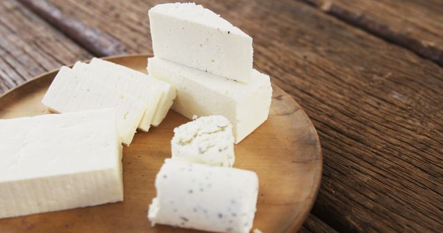A variety of fresh cheese blocks is arranged on a wooden plate. Ideal for use in food blogs, culinary websites, and promotions for gourmet restaurants. The rustic setting emphasizes organic and natural qualities, perfect for themes related to healthy eating and dairy products.