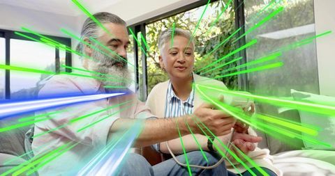 Mature couple playing game controller with neon motion trails in modern living room