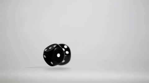 Black Dice Rolling in Slow Motion Against Grey Background