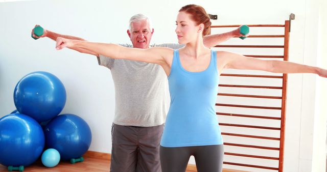 Physiotherapist showing elderly man how to lift weights at the rehabilitation center 