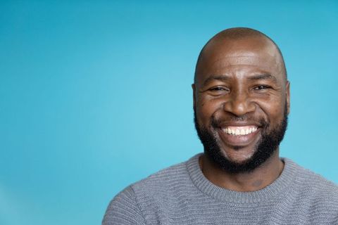 African american man smiling in gray sweater on turquoise background, closeup portrait