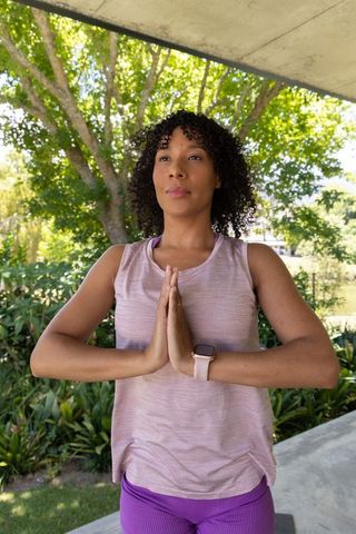 African american woman practicing mindfulness yoga prayer pose outdoors in sunlit park