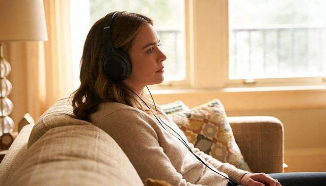 Woman listening with headphones relaxing on cozy sofa in sunlit living room