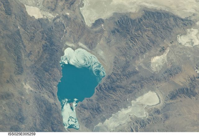 ISS025-E-005259 (28 Sept. 2010) --- Pyramid Lake in Nevada is featured in this image photographed by an Expedition 25 crew member on the International Space Station (ISS). Pyramid Lake, located in western Nevada near the California border, is a remnant of the ancient and much larger Lake Lahontan. According to scientists, Lake Lahontan formed during the last Ice Age when the regional climate of Nevada was significantly cooler and wetter than today—abundant precipitation and low rates of evaporation led to the formation of numerous lakes that began to coalesce as they overfilled their original basins. Pyramid Lake and the nearby now-dry Lake Winnemucca are two of seven lakes that formed Lake Lahontan. At its highest water level, during the late Pleistocene Epoch (approximately 15,000 years ago), Lake Lahontan covered much of western Nevada and extended into California, according to scientists. The deepest part of Lake Lahontan survives today as the perennial Pyramid Lake. Pyramid Lake is well known to geologists because of the spectacular tufa—calcium carbonate—deposits found here; the lake takes its name from one such pyramid-shaped deposit. Tufa is a rock formed by precipitation of calcium carbonate from spring water, lake water, or a combination of the two. Over time, these deposits can develop a wide variety of forms including mounds, towers, sheets, reefs and coatings on other rocks. These may then be exposed when the water level drops due to changes in regional climate, diversion of water for human use, or both (Mono Lake in California for example). This photograph also captures sunglint—light reflected off of a water surface back towards the observer on the space station—on the northern and southeastern ends of the lake. Two large spiral whorls are visible in sunglint at the northern end of the lake; these likely trace surface wind patterns disturbing the water surface that cause localized variations in the amount of light reflected back to the ISS.