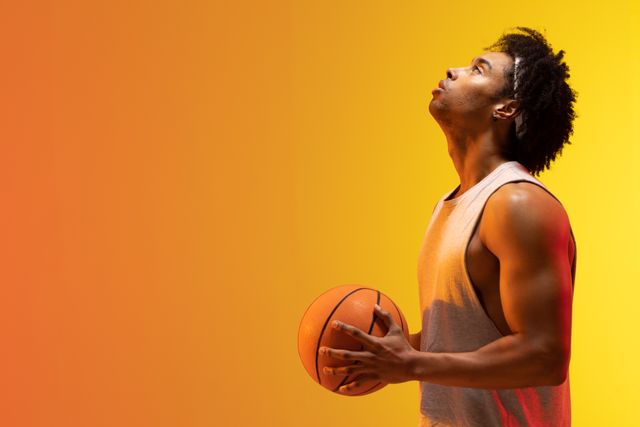 Side on of african american male basketball player with ball looking up, in orange light, copy space. Athlete, sport, competition, confidence and fitness concept.