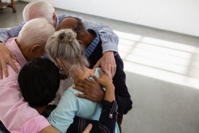 Senior friends are seen embracing in a group huddle, symbolizing unity and support. This image can be used to represent themes of friendship, community, and togetherness among the elderly. It is ideal for use in advertisements for senior care services, community centers, and social interaction programs for seniors.