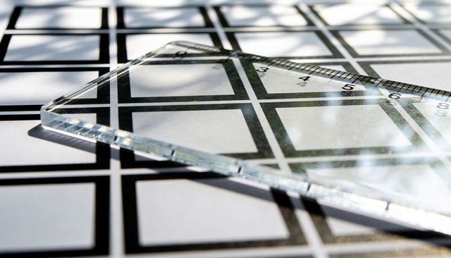 Acrylic ruler resting diagonally on calibration grid casting reflections shadows and glare