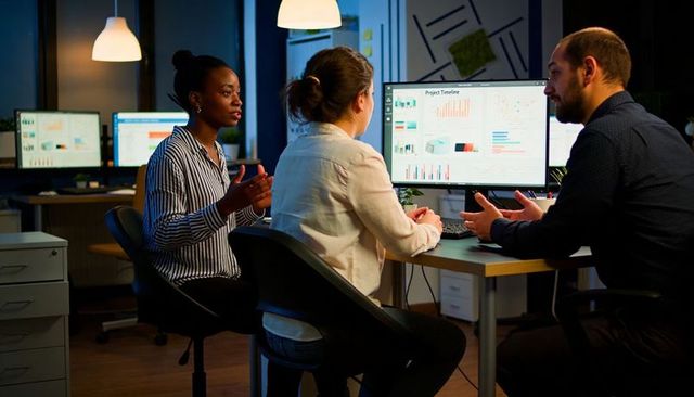 Team reviewing project timeline on desktop monitor, collaborating on charts and data