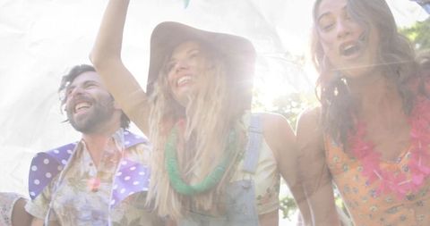 Friends singing and cheering at outdoor summer festival with sun flare and denim overalls