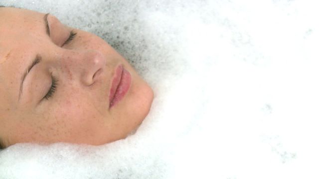 A peaceful depiction of a woman relaxing with her face partially submerged in soothing bubbles. This can be used in spa advertisements, wellness campaigns, or lifestyle content to highlight themes of relaxation, rejuvenation, and self-care.