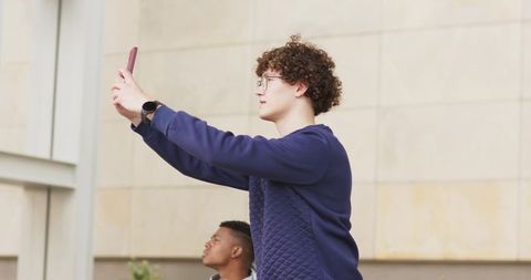 Young diverse friends standing in urban courtyard taking selfie with pink-case smartphone