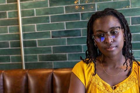 Contemplative african woman wearing glasses in mustard blouse at cafe booth
