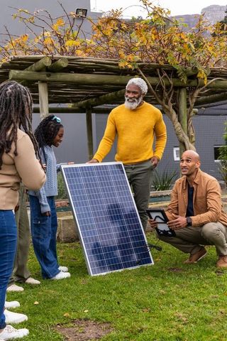 Multigenerational family learning about solar panel in backyard garden with pergola