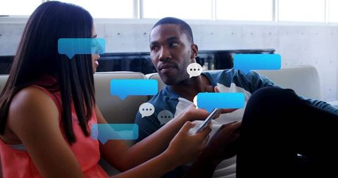 Couple sharing smartphone on sofa surrounded by digital chat bubbles illustrating messaging