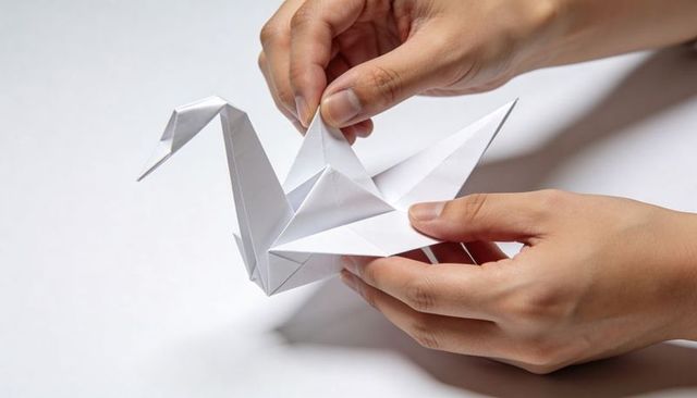 Hands holding and adjusting white origami crane on minimal white tabletop