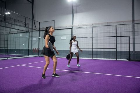 Female doubles playing padel on purple court, teammates practicing in sporty dresses