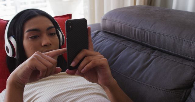 Biracial gender fluid person sitting on couch using smartphone and listening to music at home - Download Free Stock Photos Pikwizard.com