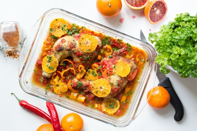 Perfect for food blogs, recipe websites, and cooking magazines, this image showcases a beautifully prepared dish of baked chicken legs garnished with orange slices and fresh herbs, accompanied by chili peppers and parsley. Good for culinary tutorials, healthy eating promotions, or restaurant menus.