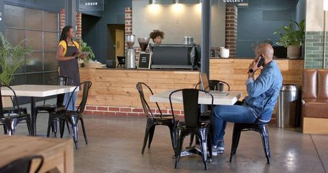 African american barista serving coffee while customer talking on phone in modern cafe