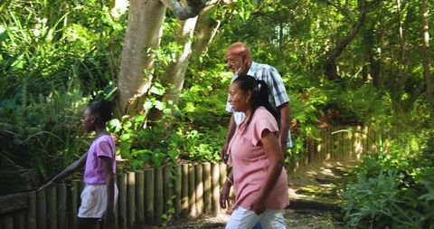 Senior couple walking with granddaughter on wooded trail in nature park