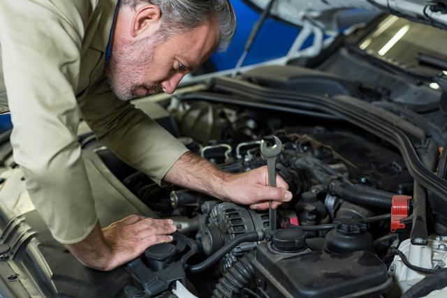 Mechanic servicing car engine using a wrench in a professional auto repair shop. Ideal for content related to car maintenance, mechanical services, automotive industry, technical skills, and professional expertise.