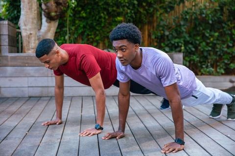 Young Men Planking Outdoors with Smartwatches on Wooden Deck
