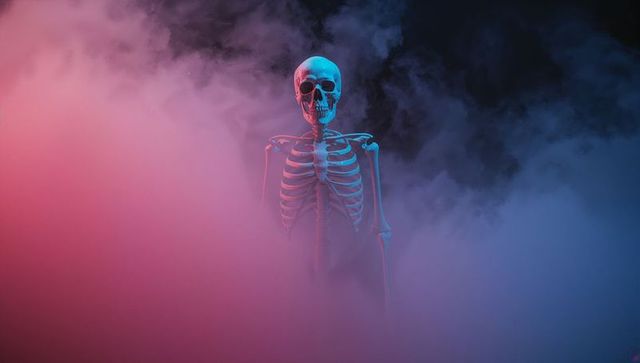 This art evokes drama with a stark skeleton brightly lit by red and blue lights amidst dense colored fog. It captures an eerie and surreal scene, perfect for providing a mysterious ambiance in theatrical productions, Halloween promotions, or creative artistic projects seeking a dramatic flair.