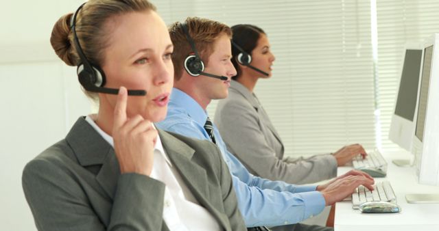 Caucasian business professionals are working in a call center environment, with copy space. They are wearing headsets and focused on assisting customers through their computers.