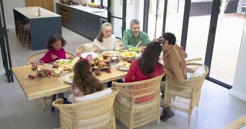 Multi-generation family sharing holiday meal around wooden table in sunlit kitchen