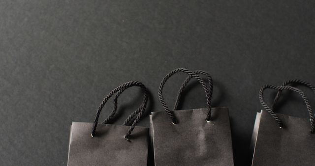 Three black gift bags with black handles in a row on dark grey background with copy space. Luxury treat, present, shopping, black friday sale and retail concept digitally generated image.
